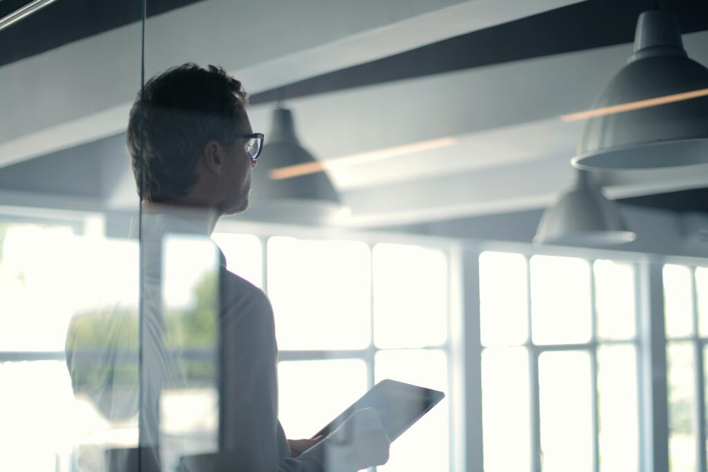 pexels photo 3760093 3760093 A businessman holding a tablet in an office, looking thoughtfully through a glass wall.